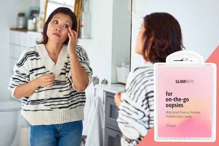Woman examines face in mirror, wearing striped sweater in a bright room. Nearby, Glamnetic makeup remover packaging reads, 