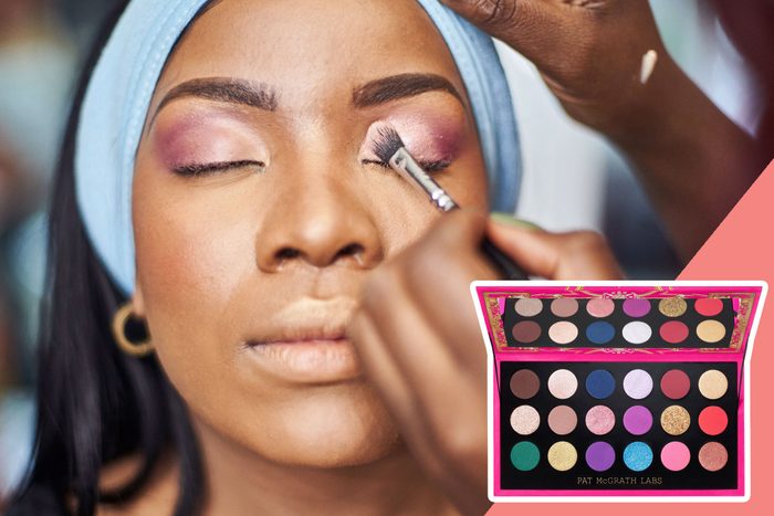 A woman with closed eyes receives pink eyeshadow application, wearing a blue headband. A colorful eyeshadow palette is displayed inset at the bottom.