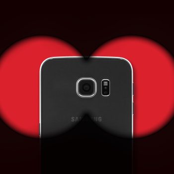 A smartphone viewed through red-tinted binoculars, centered in a dark background.