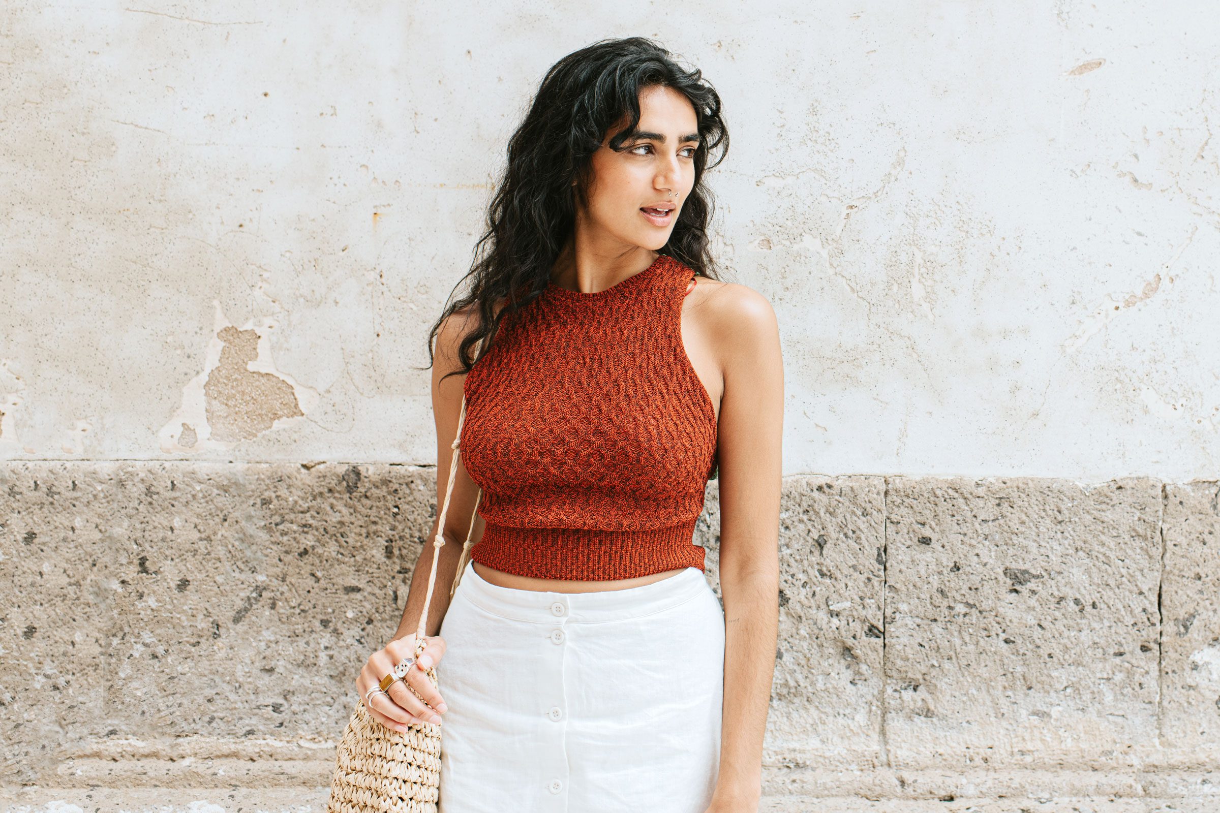 A stylish, elegant young woman with a small bag, stands outside, gazing off to the side