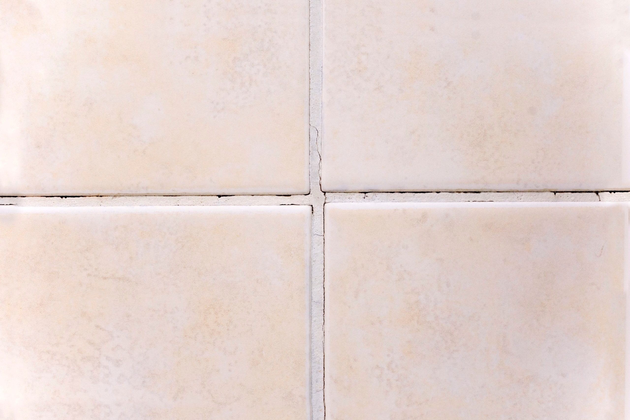 Four beige ceramic tiles, evenly arranged with visible grout lines, form a grid pattern. Subtle speckled texture enhances the surface appearance.