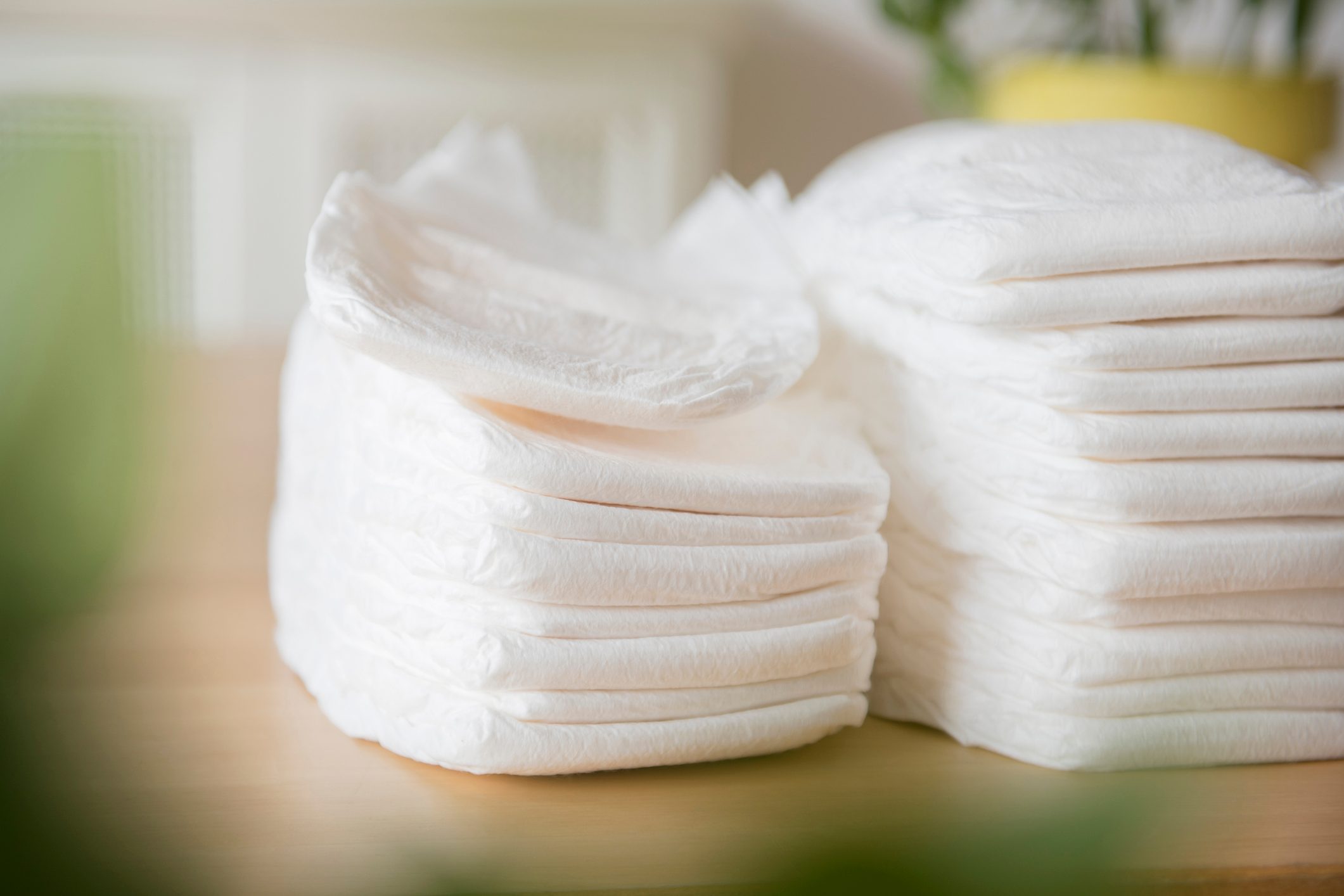 Stacks of white diapers sit neatly arranged on a wooden table, with blurred greenery in the background.
