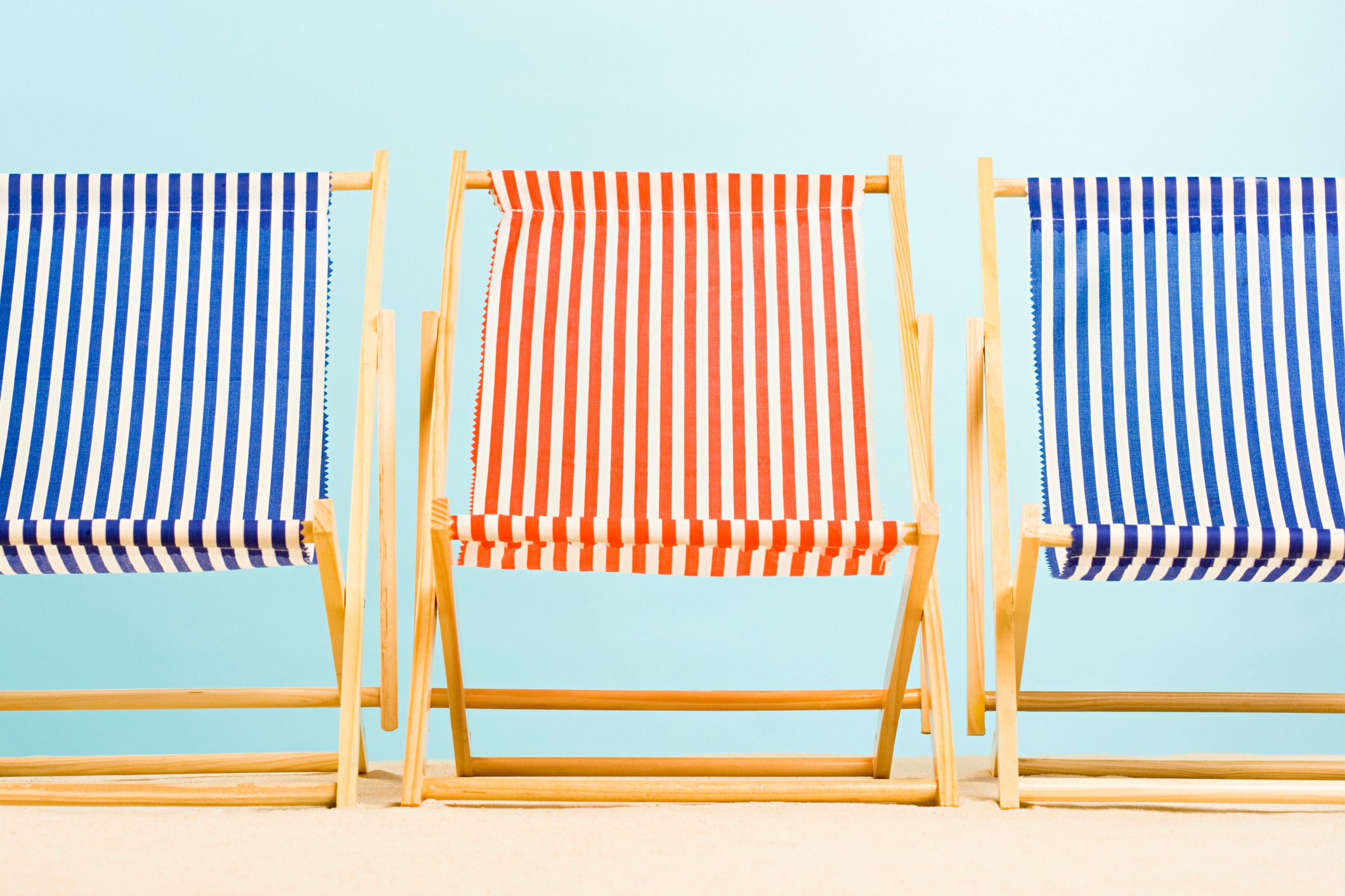 Chairs sit in a row; red and blue striped design, on a sandy surface with a light blue background.