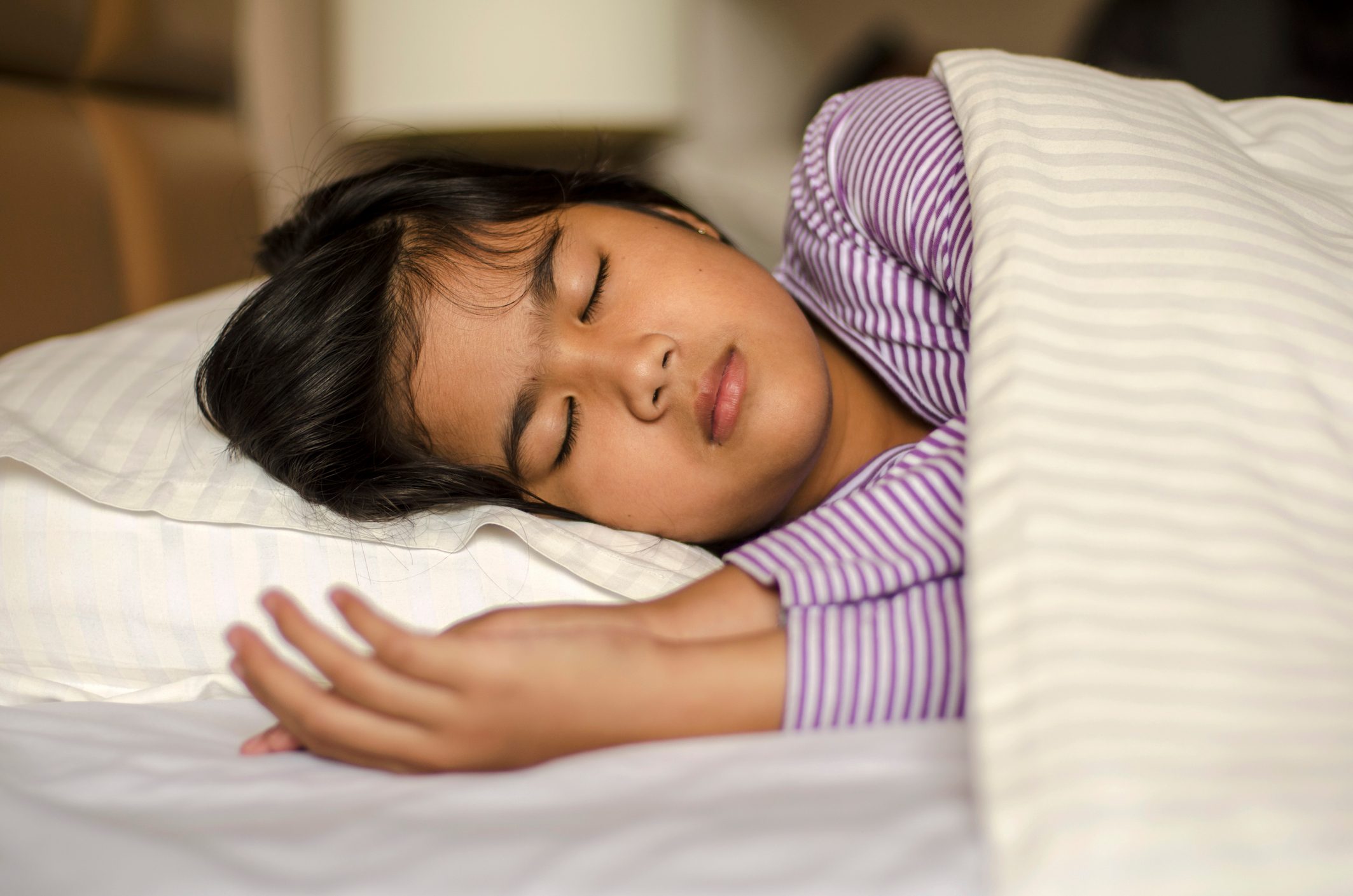 A child sleeps peacefully on a bed, wearing striped pajamas, under a striped blanket in a cozy bedroom setting.