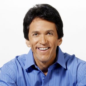 A person smiles warmly, wearing a blue, striped shirt against a plain white background.