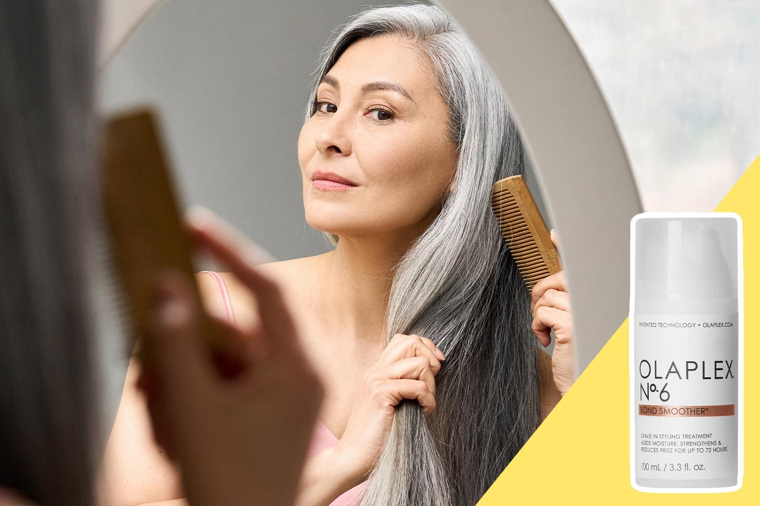 A woman combs her long gray hair while looking in a mirror; OLAPLEX No.6 Bond Smoother product displayed beside her.