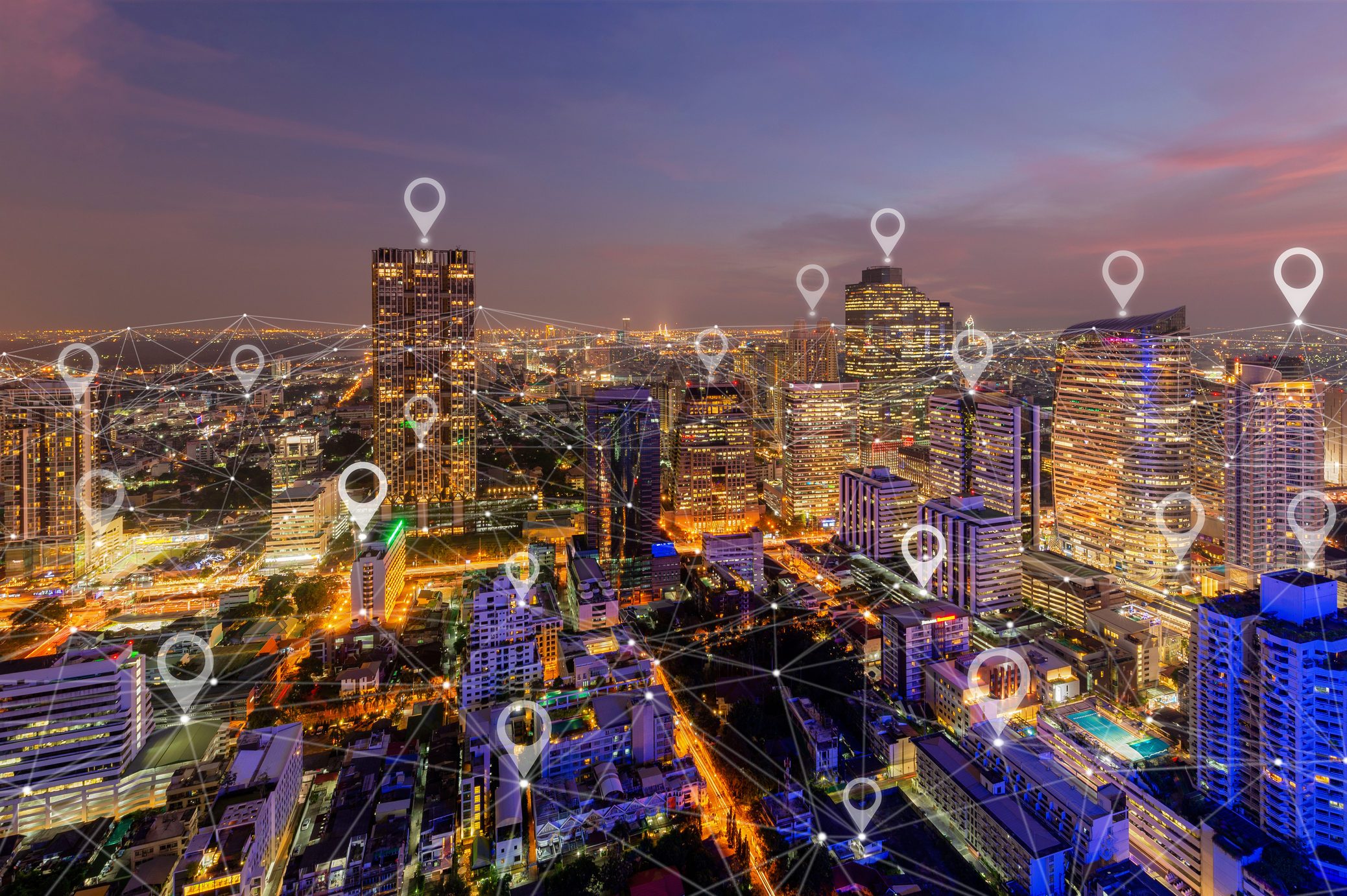 Cityscape shows illuminated buildings with digital location markers connected by lines, indicating a networked, technology-driven urban environment at dusk.