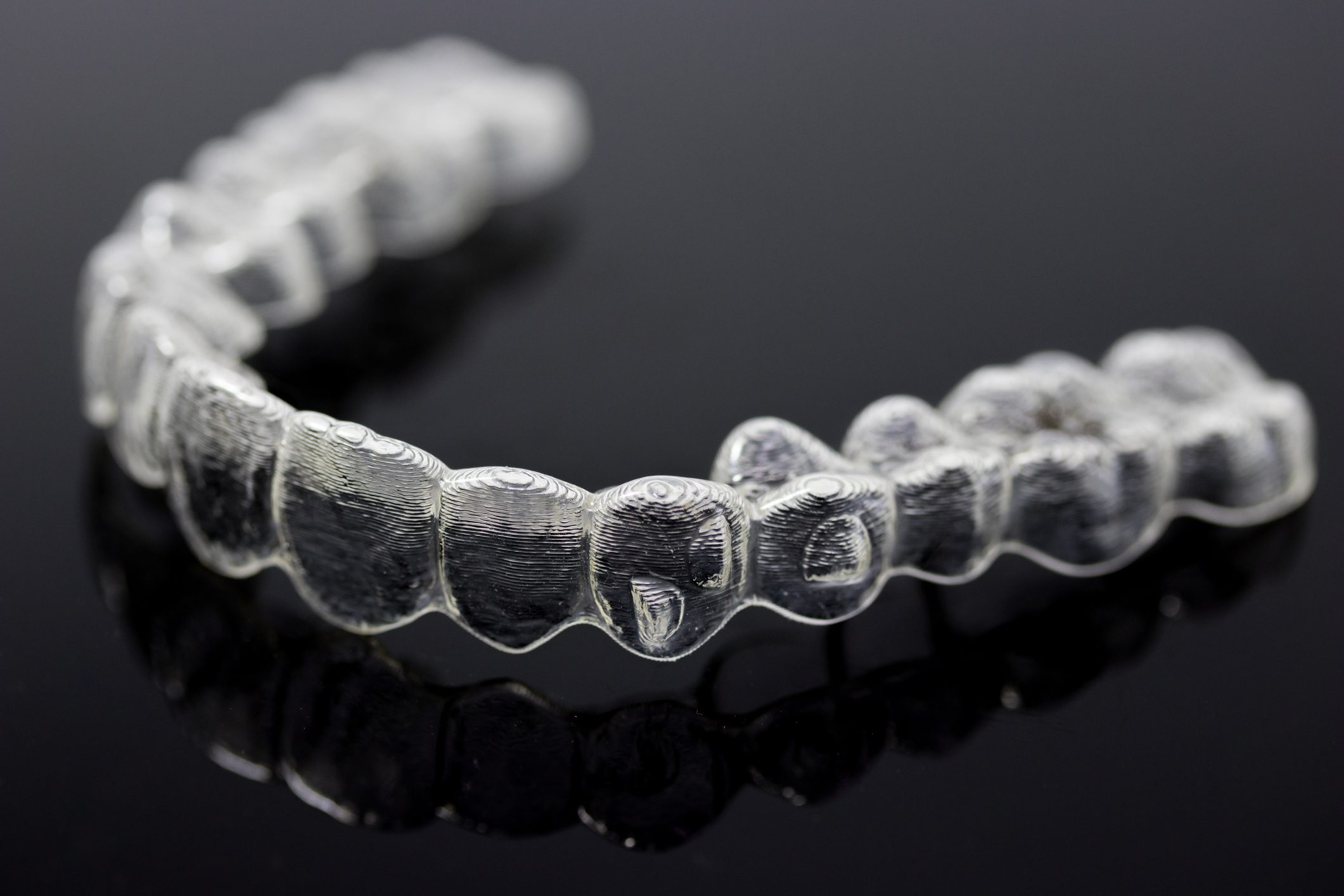 A clear dental aligner rests on a reflective black surface, showcasing its detailed tooth imprints and smooth, curved structure.