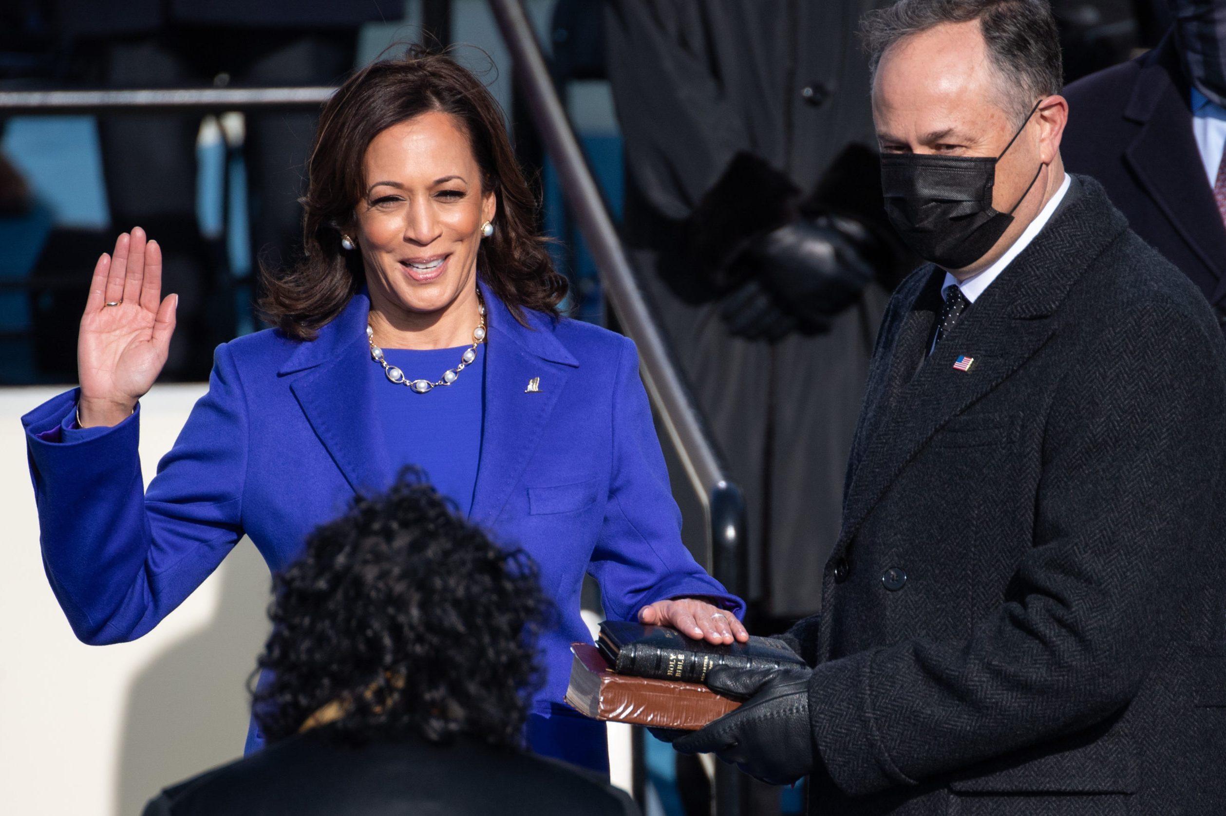 A woman raises her right hand, taking an oath, surrounded by people in formal attire on a stage.