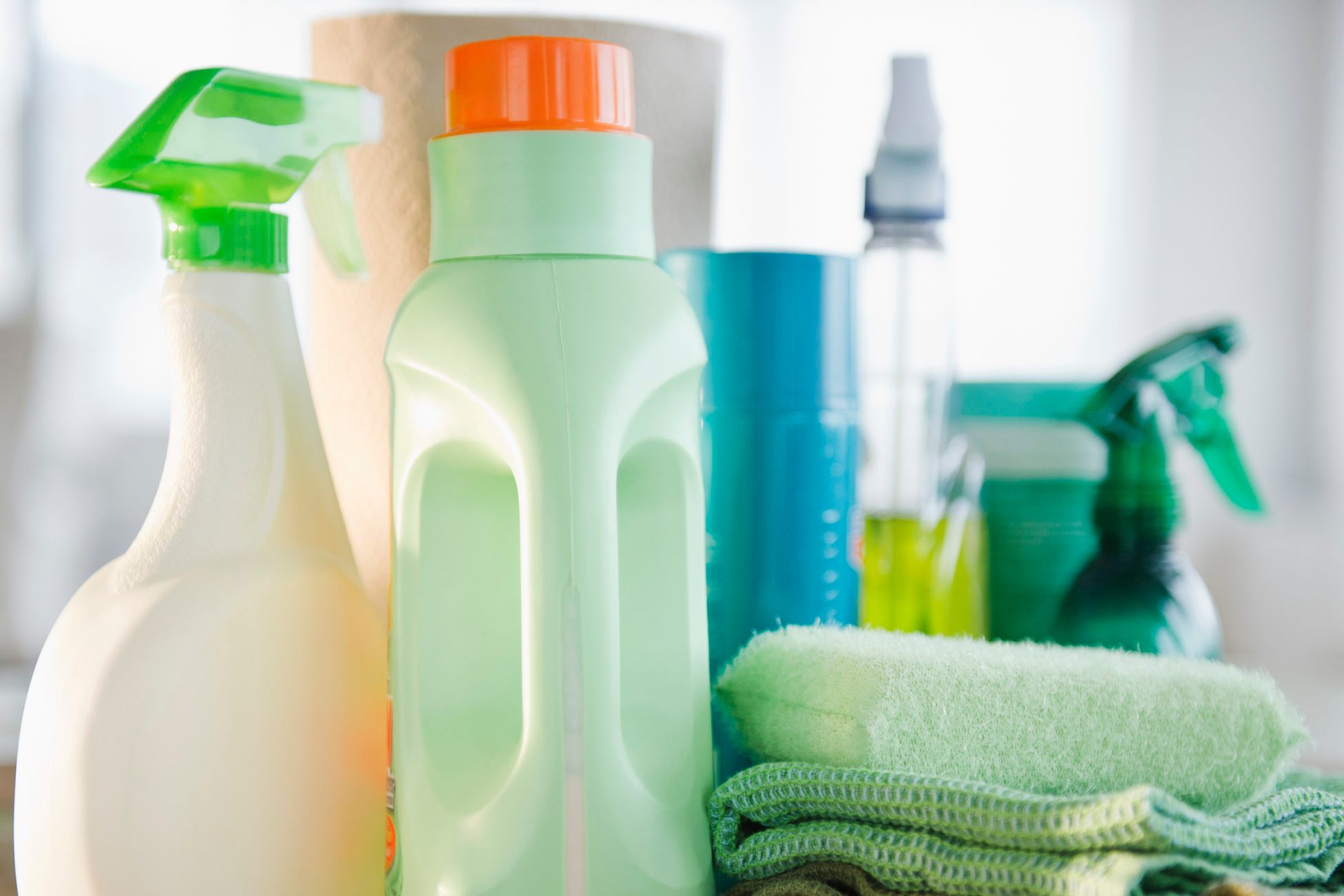 Cleaning bottles stand together, surrounded by towels and paper, in a bright, domestic setting.