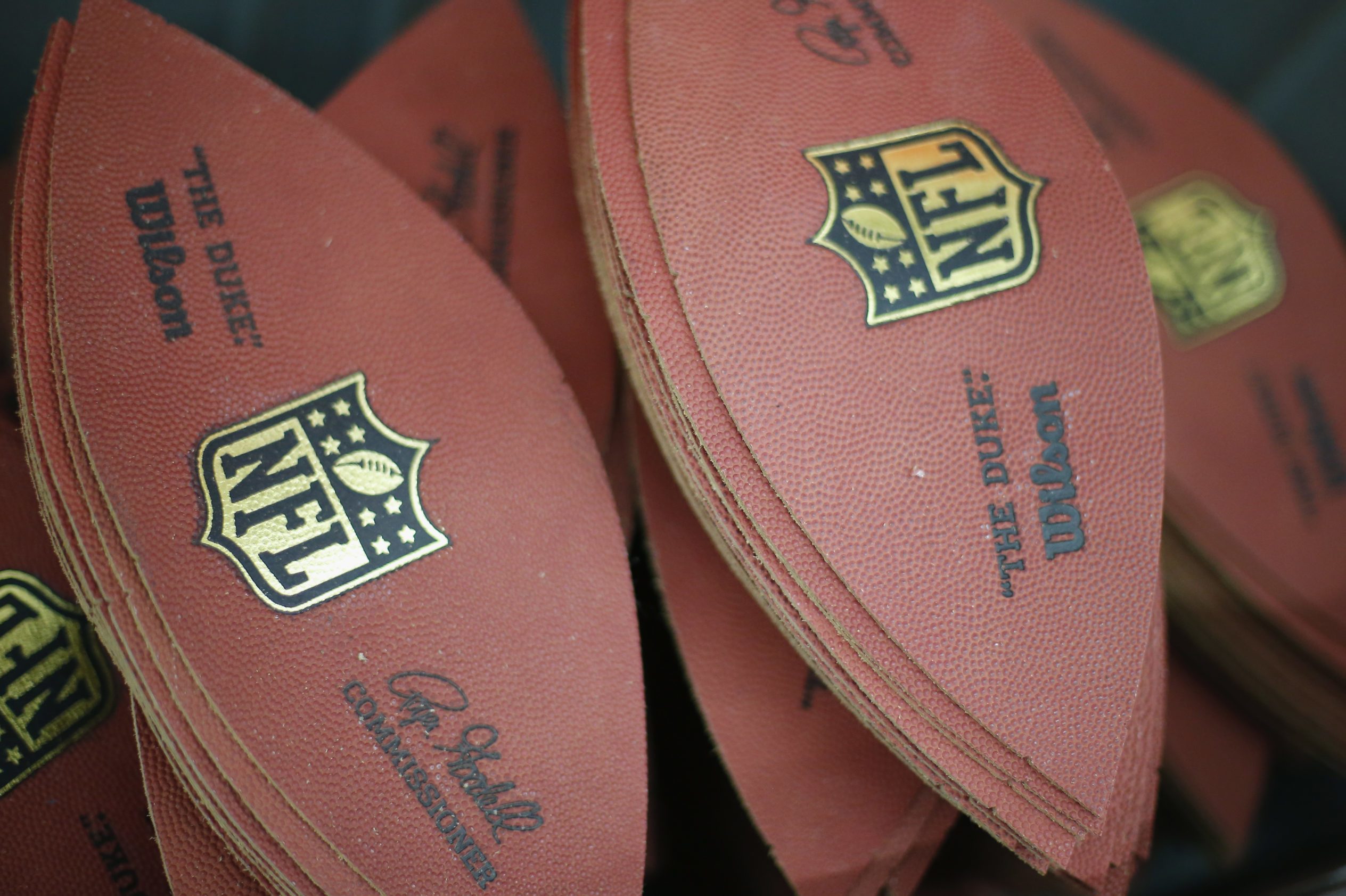 Peel-shaped leather panels stacked, featuring "NFL" logo and text "The Duke" Wilson, in a manufacturing setting.