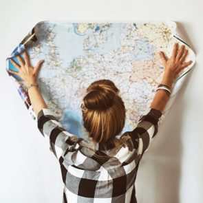 Person unrolling a world map; hands spread wide against a wall, wearing a black and white checkered shirt.