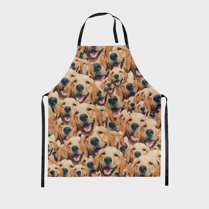 An apron displays repeated images of smiling golden retrievers, arranged close together, creating an energetic and cheerful pattern against a plain background.