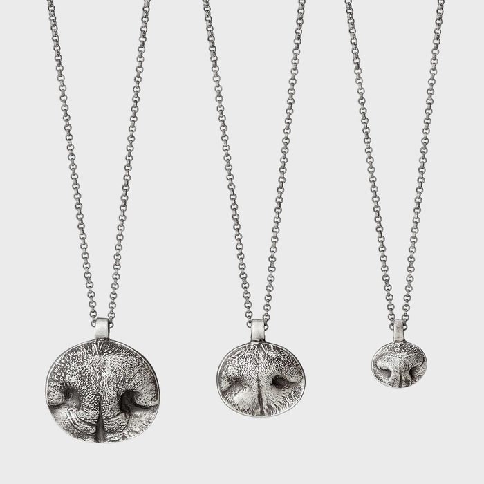 Three silver necklaces hang vertically, featuring pendants shaped like dog noses, displayed against a plain, light background.