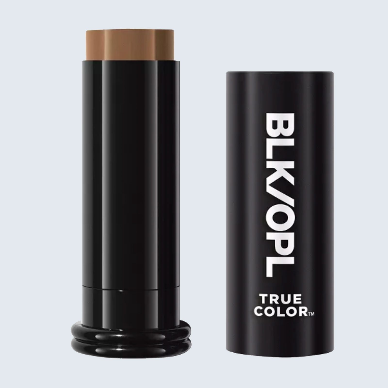 A cylindrical black makeup stick stands upright, with a brown product exposed, beside a matching cap labeled "BLK/OPL TRUE COLOR" in a minimal setting.