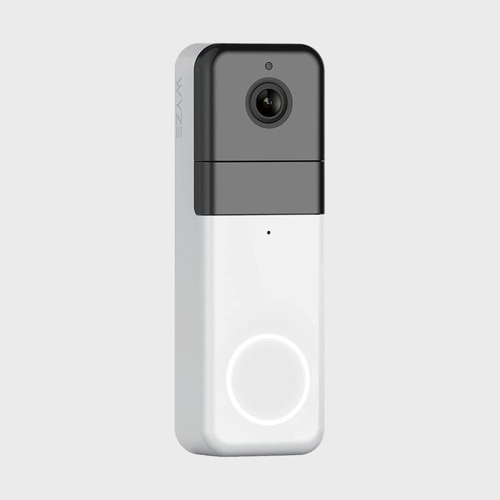 A rectangular video doorbell, gray and white, positioned against a neutral background, with a camera lens at the top and a button below.