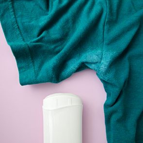 A teal shirt lies on a pink surface beside a white deodorant stick, suggesting freshness and cleanliness.