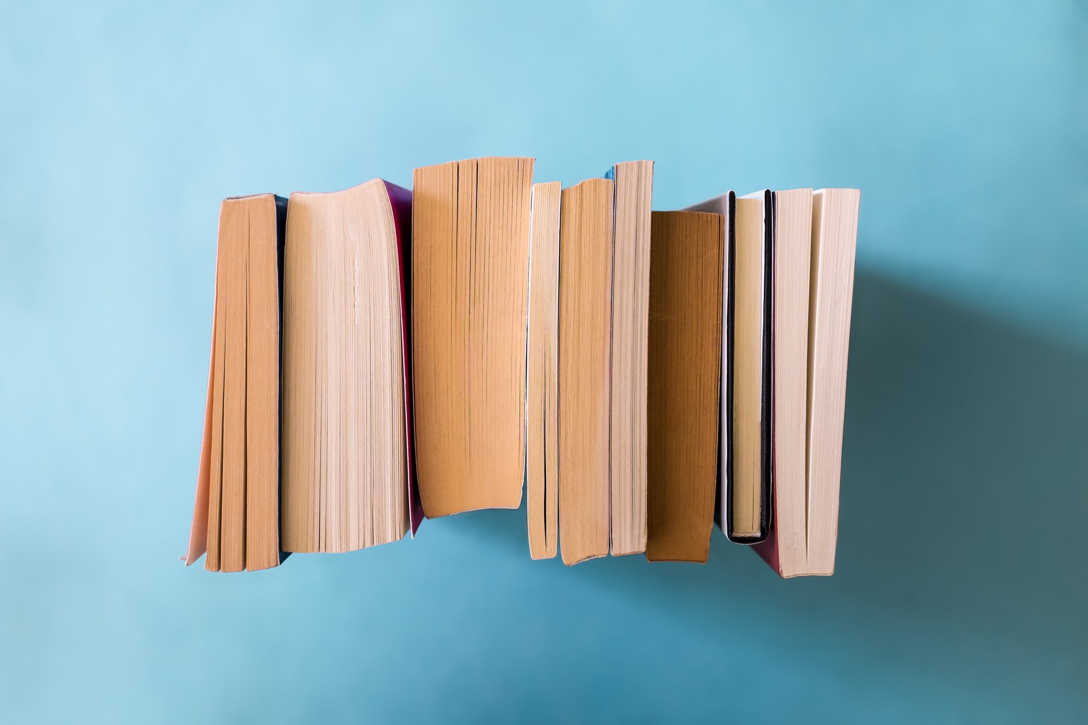 Books stand upright with pages facing outward against a solid blue background, edges slightly unevenly aligned.