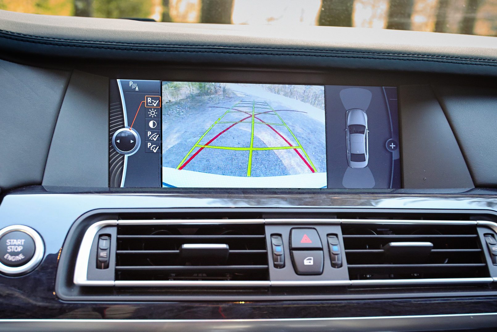 Dashboard screen displays a rear-view camera image with parking guidelines. Surrounding car controls are visible, including buttons for hazard lights and locking.