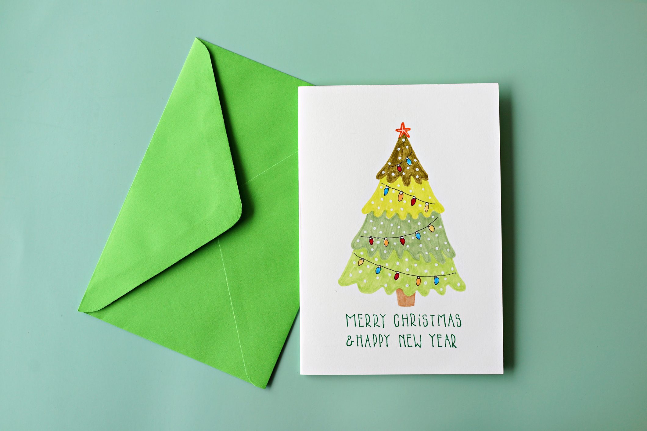 Card displays a decorated Christmas tree; text below reads "Merry Christmas & Happy New Year." Green envelope lies beside it, on a green background.
