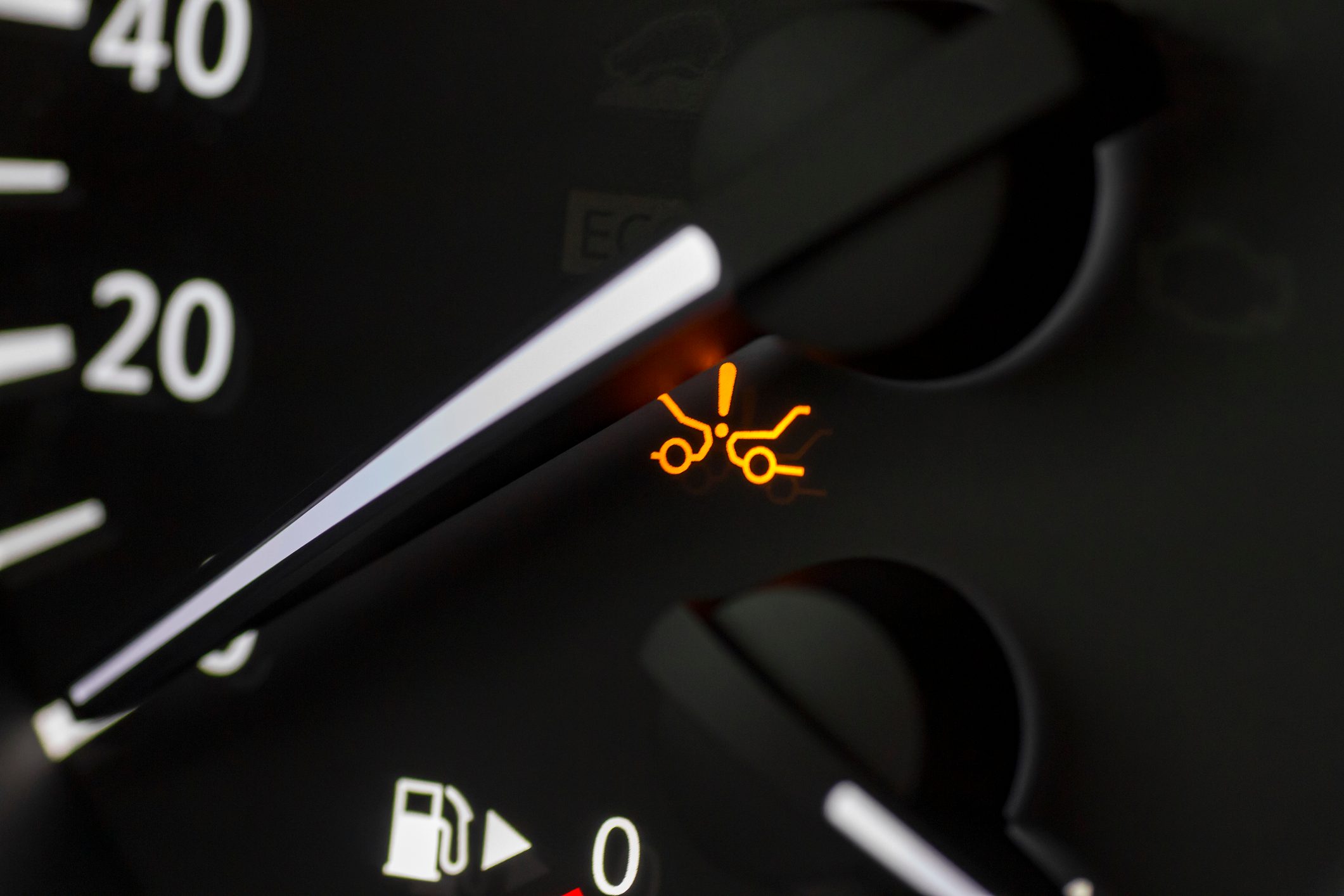 Car dashboard shows a collision warning light illuminated, surrounded by speedometer gauge and fuel indicator in a dimmed cockpit environment.