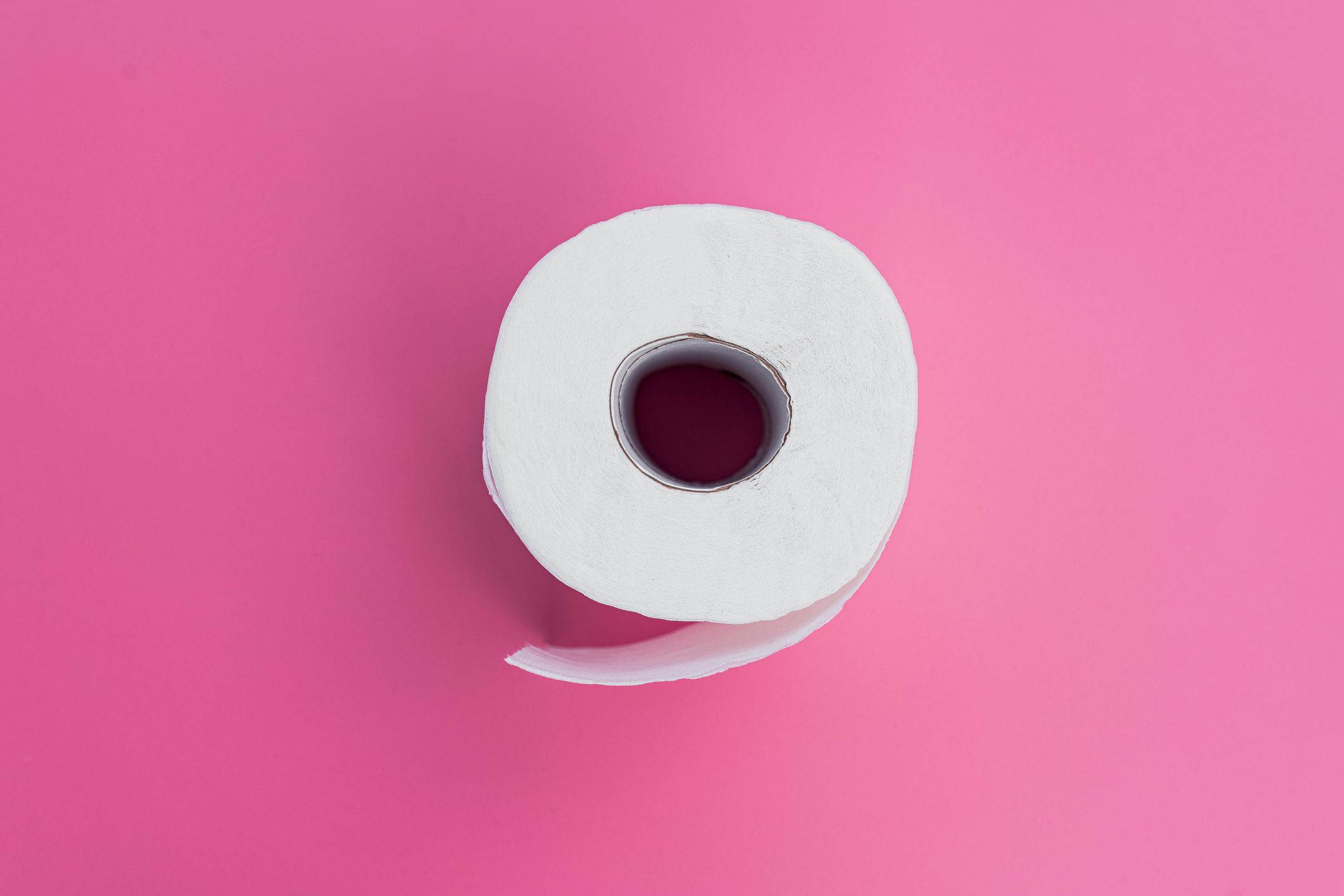 A roll of toilet paper sits on a bright pink background, with one sheet slightly unrolled.