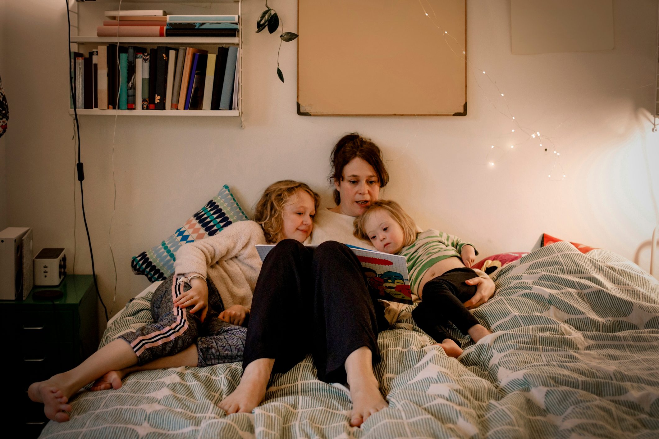 Full length of mother reading picture book while sitting with children in bedroom