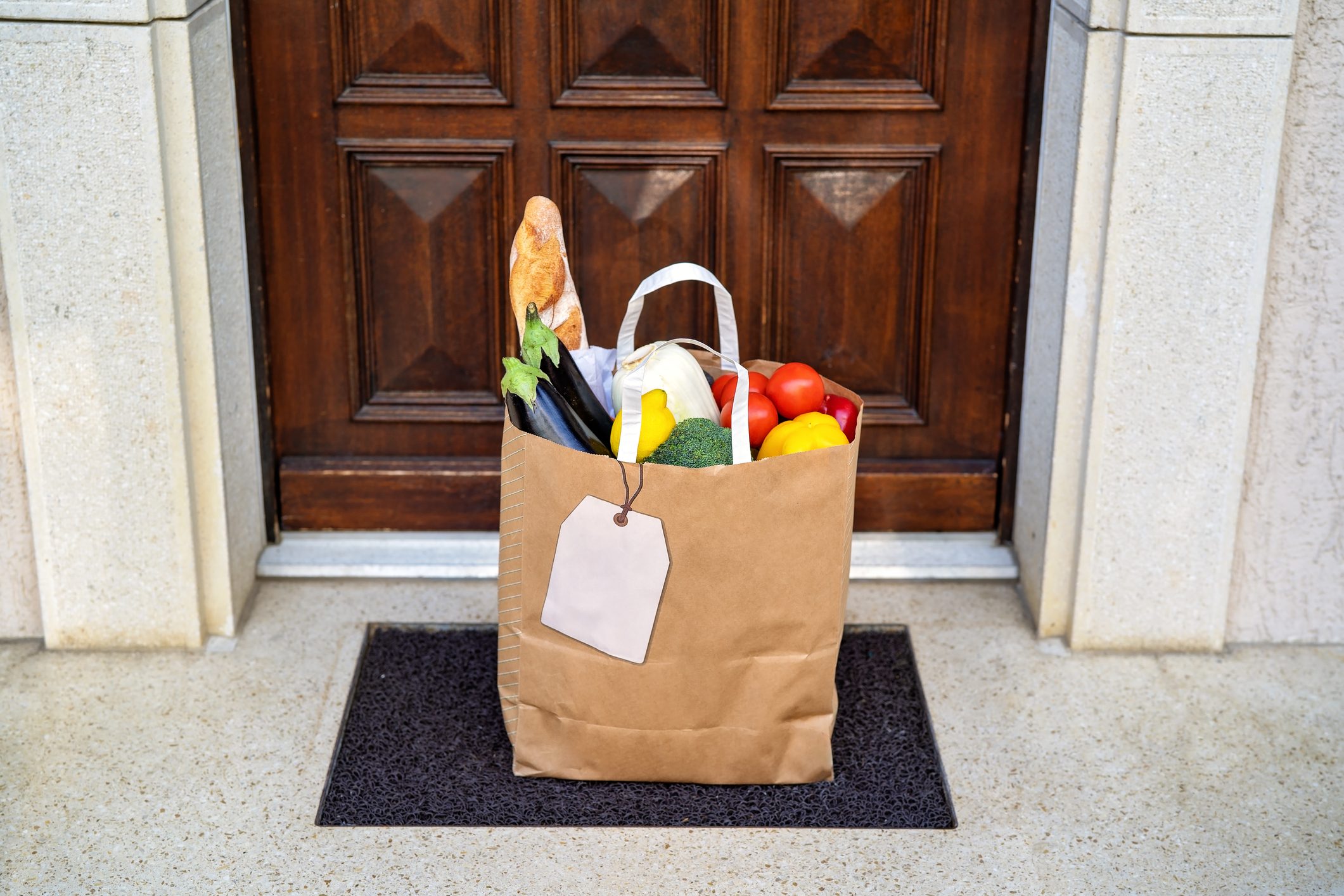 Contactless food delivery service concept. Paper bag with groceries delivered and left outside at entrance door. Online shopping. Healthy fresh fruit and vegetables, zero waste, recyclable package.