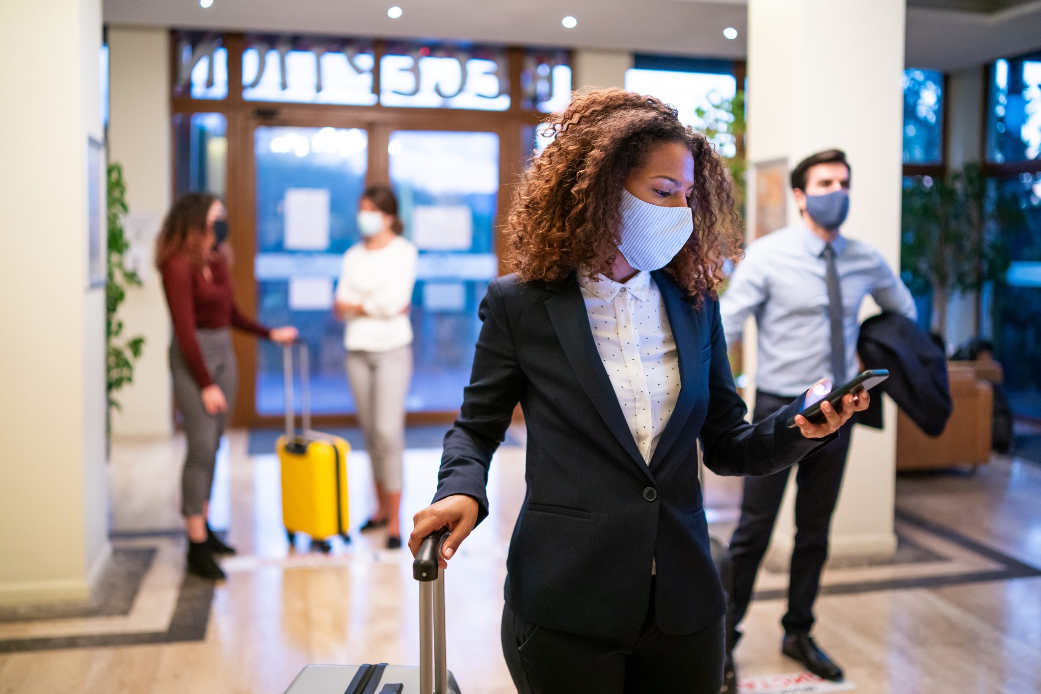 Hotel guests wearing face masks in the lobby; one woman is checking in on her smartphone