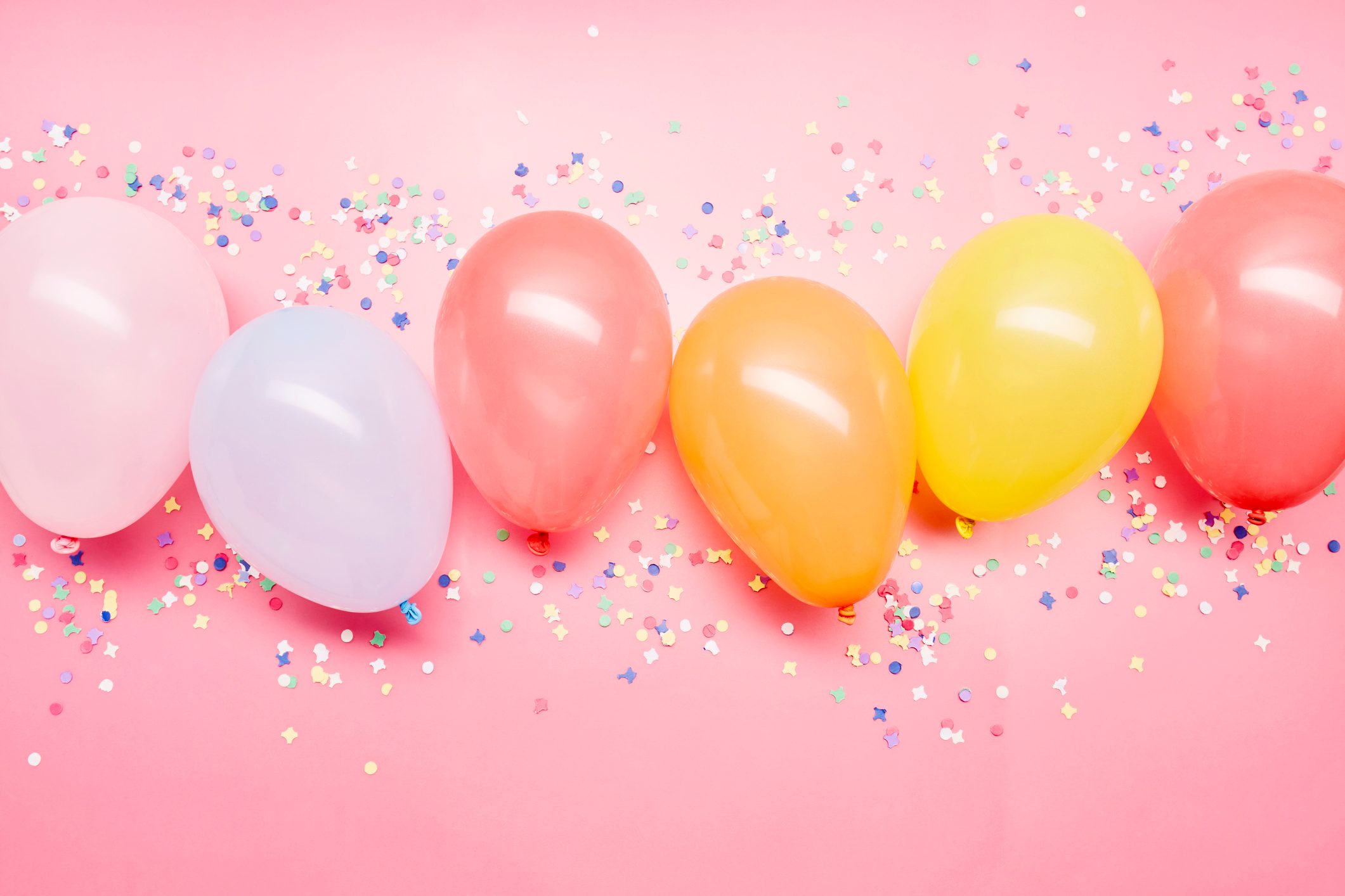Colorful balloons lay on a pink surface, surrounded by scattered multicolored confetti.