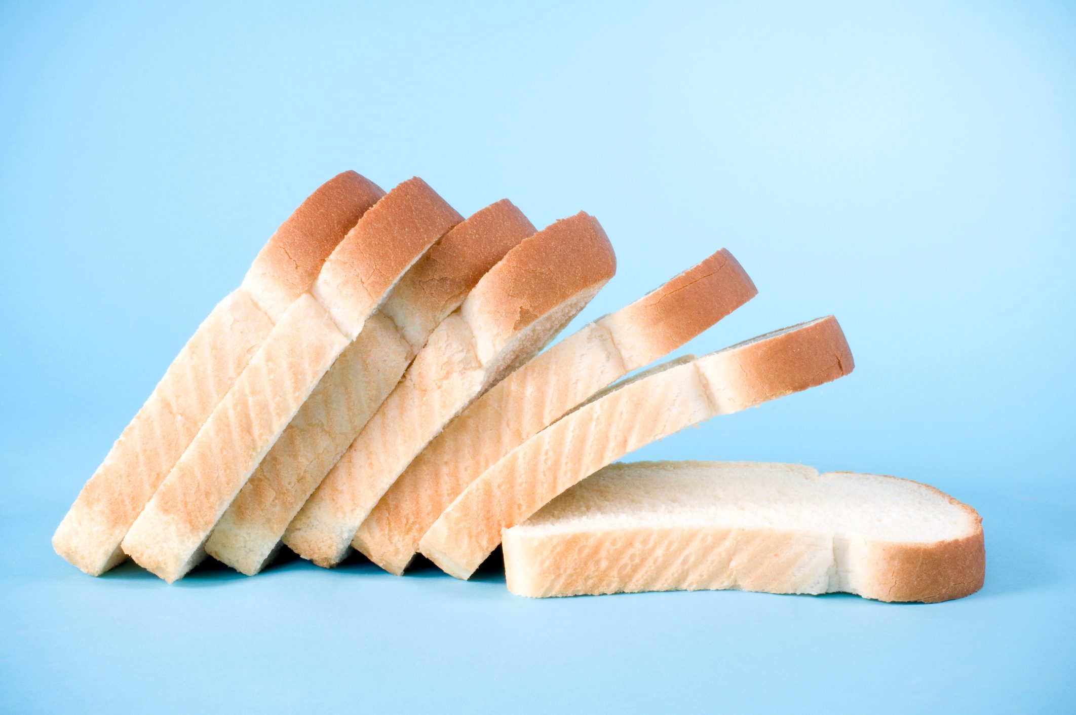 Slices of white bread lean diagonally on each other against a light blue background.