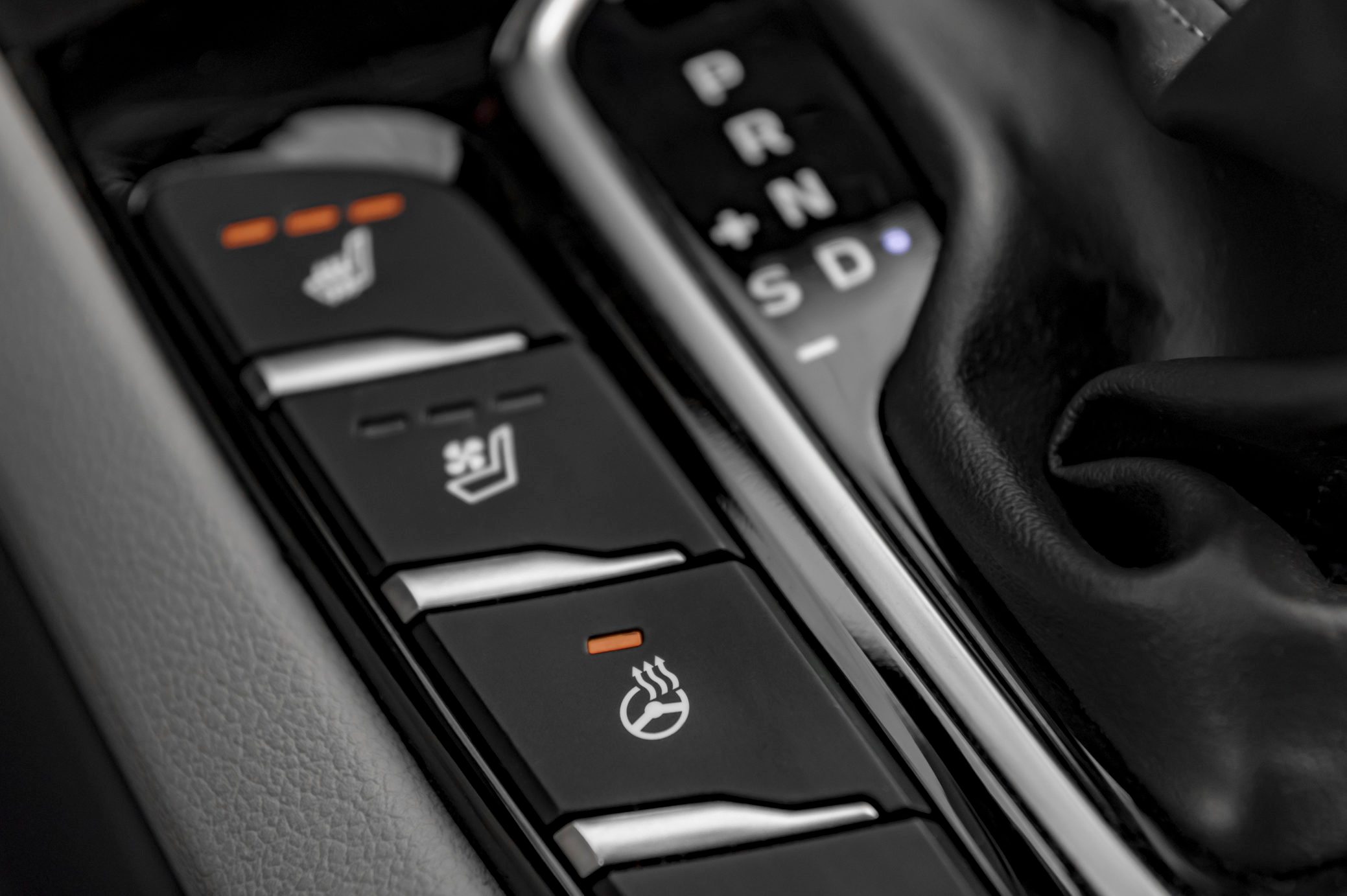 Buttons activate heated seats, steering wheel in a car interior alongside gear shifter display "P R N D S + -".