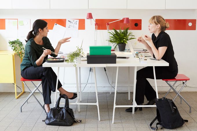 Full length of businesswomen talking while having lunch at table in office