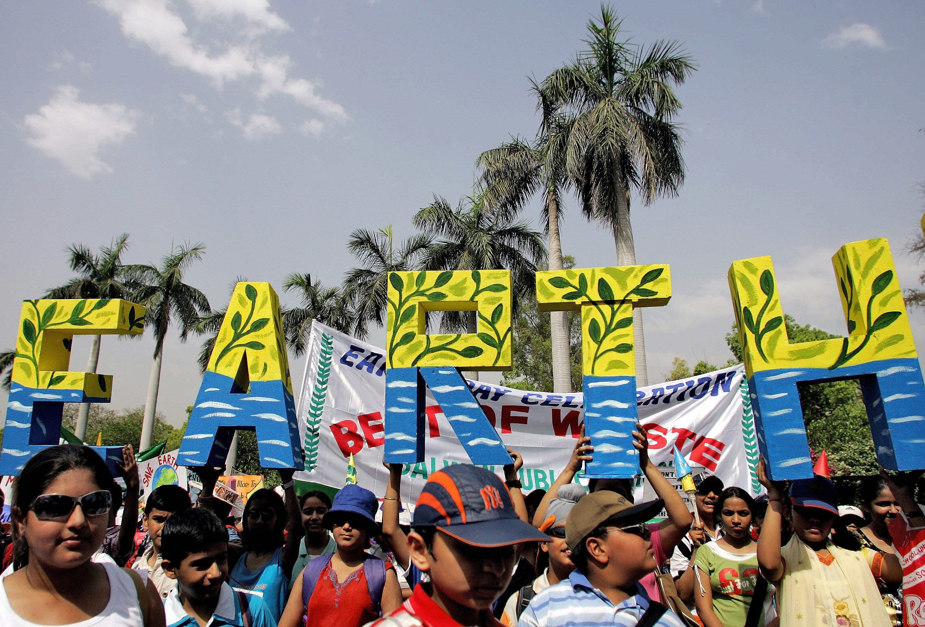 Participants hold large "EARTH" letters during a festive outdoor event surrounded by palm trees, conveying an environmental or celebratory theme.