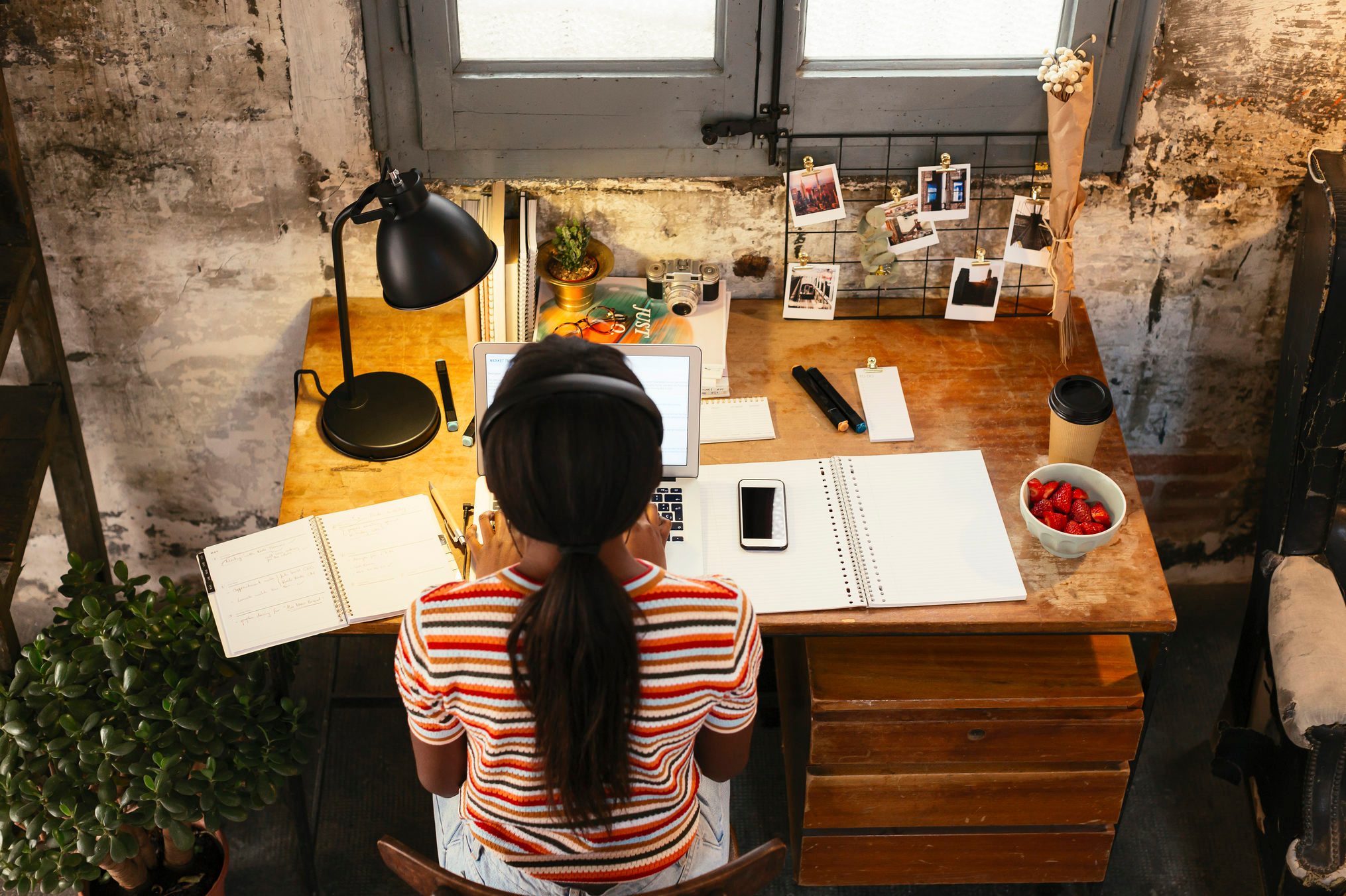 Back view of young woman sitting at desk in a loft working on laptop seen from above