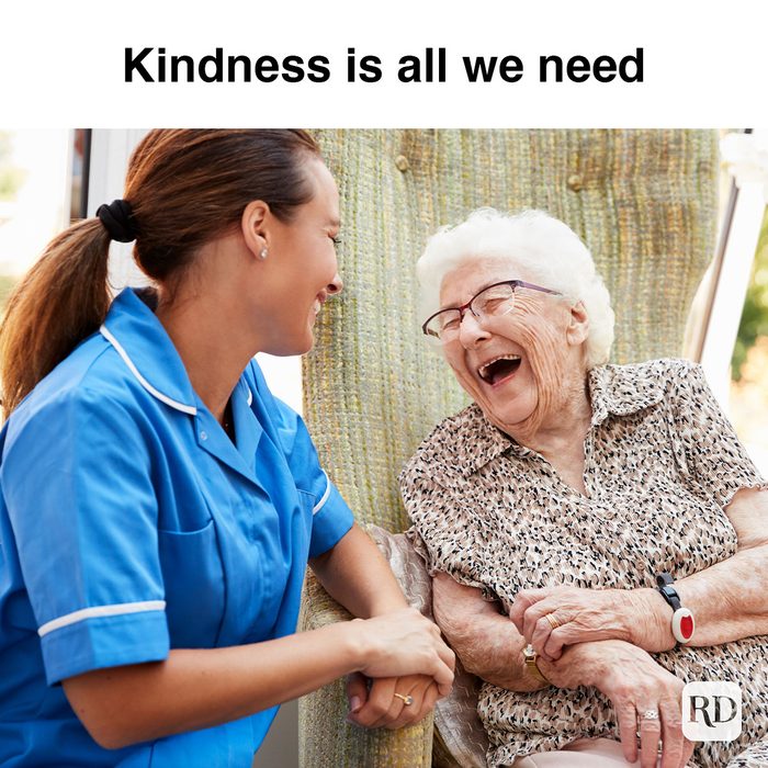 Senior Woman Sitting In Chair And Laughing With Nurse In Retirement Home