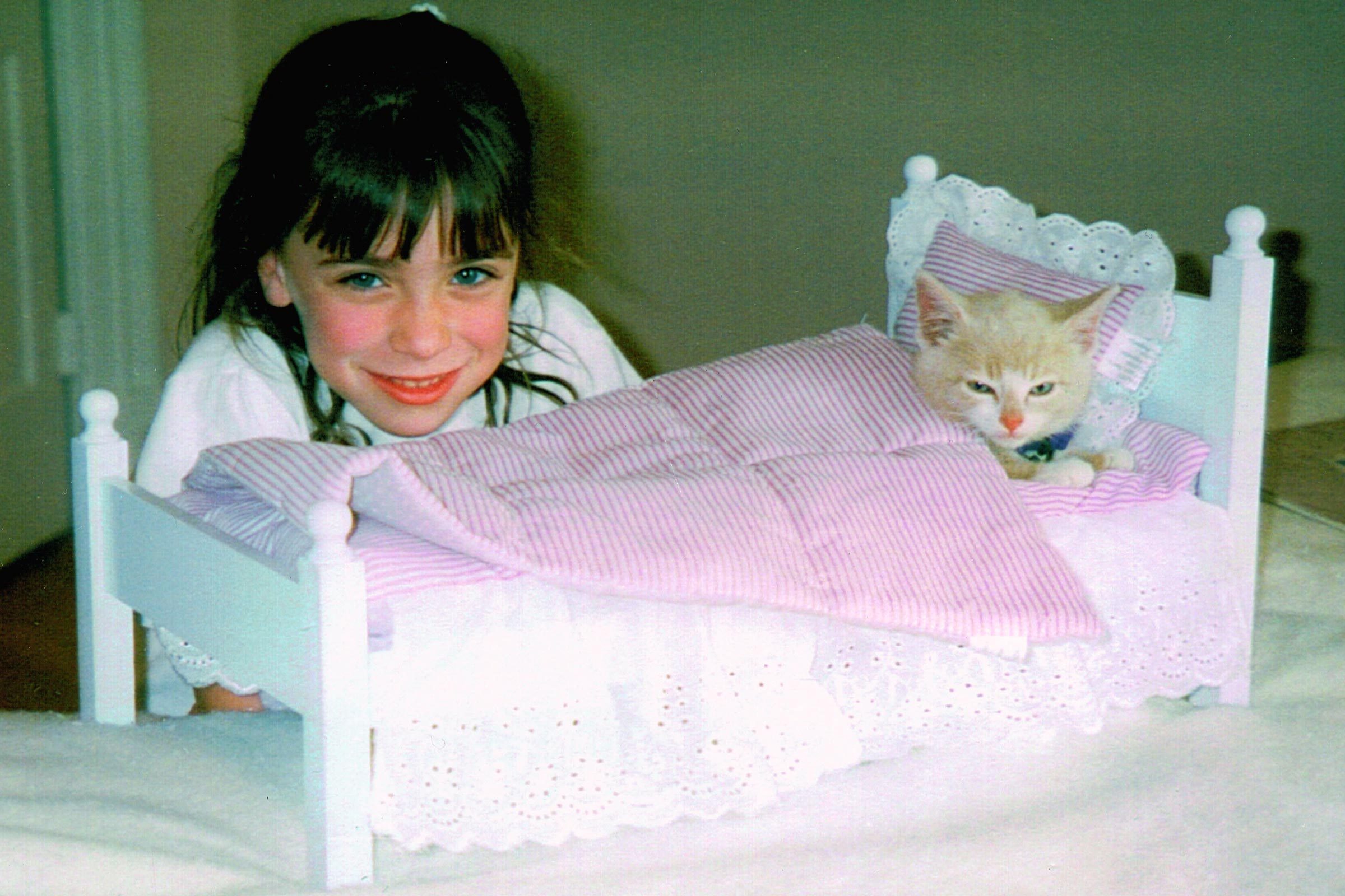 little girl with a kitten in a doll bed