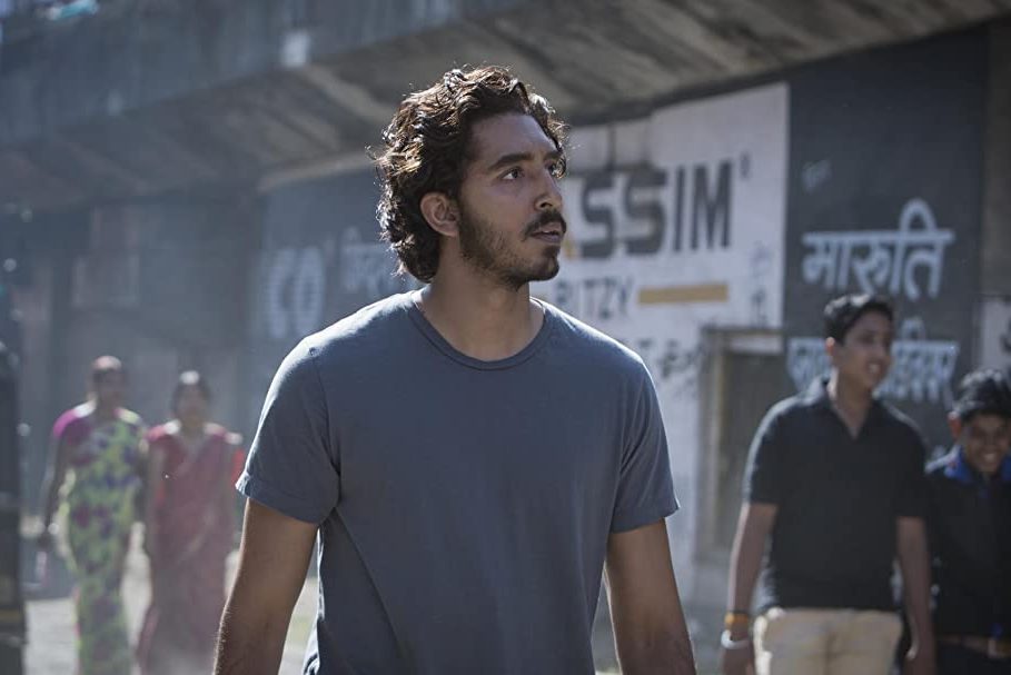 A person walks on a bustling street with people and walls covered in signs and advertisements.