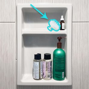 Bathroom shelf holds three bottles below and an illustrated arrow pointing to a scalp brush and a small dropper bottle above.