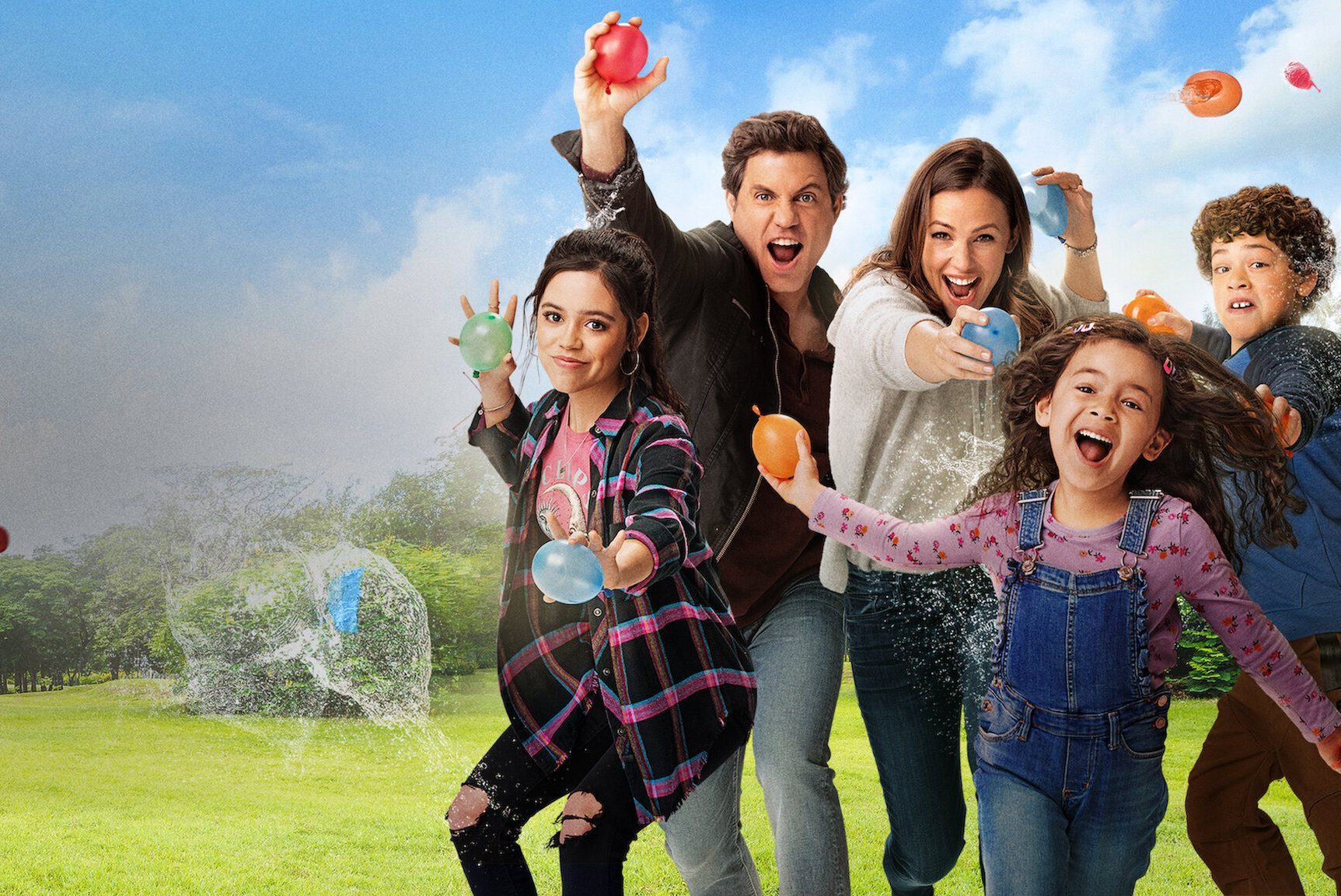 Group throws water balloons playfully in a sunny park, with trees in the background.