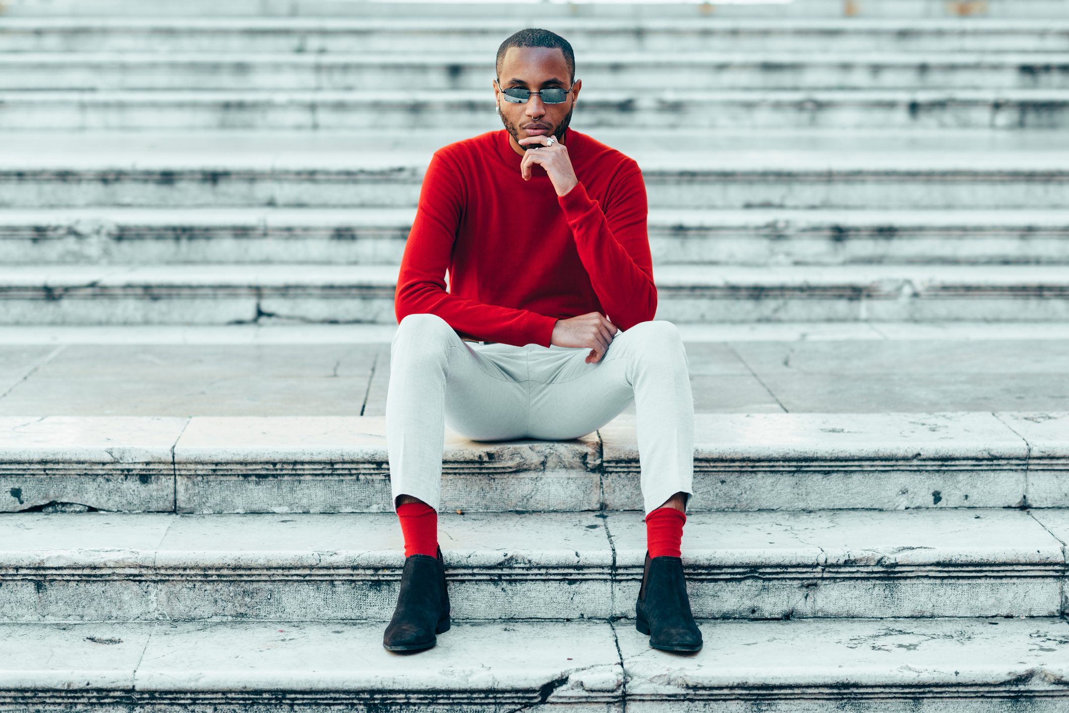 Portrait of stylish young man wearing red pullover and socks sitting on stairs
