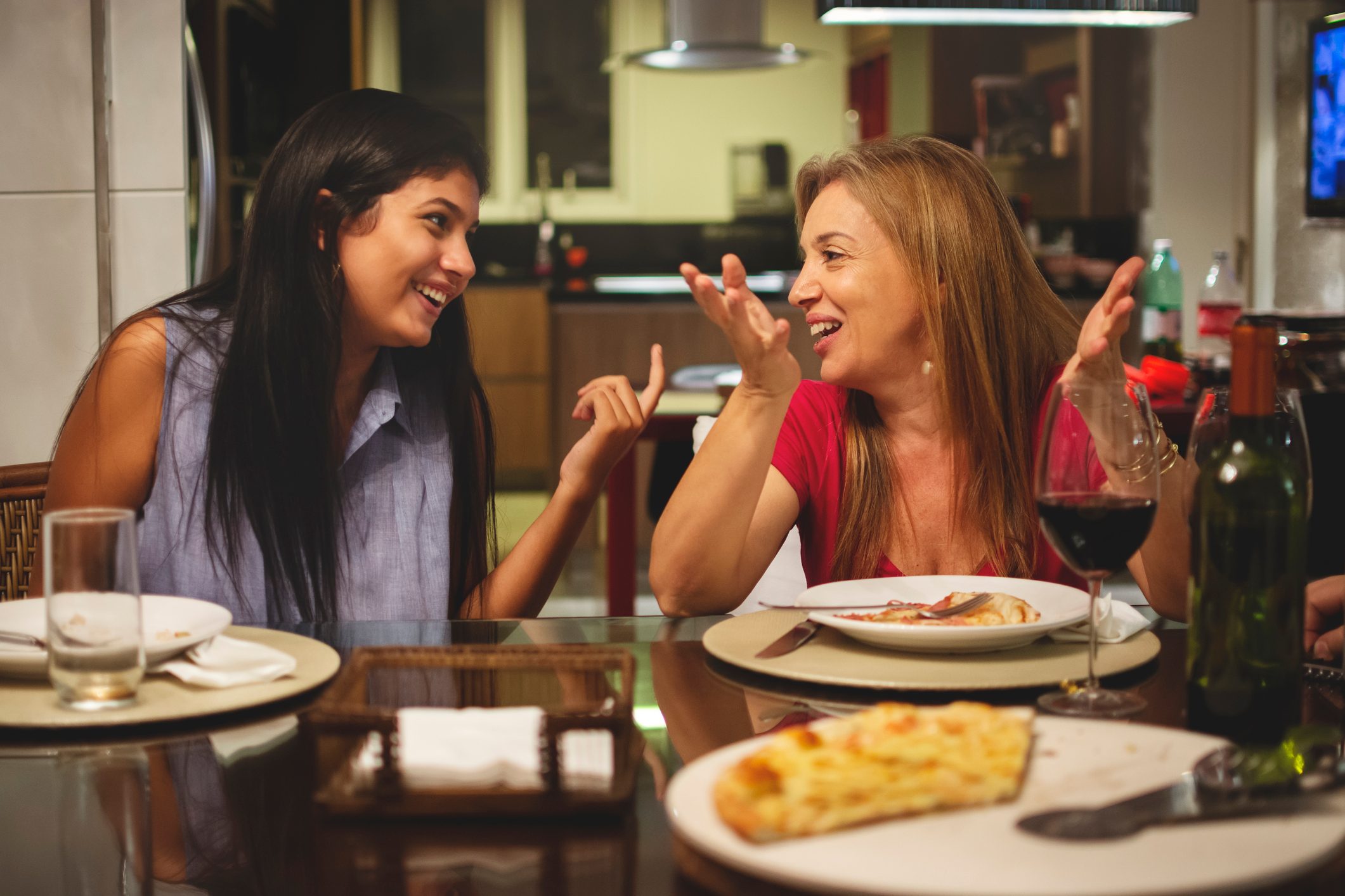 Mother and daughter eating pizza together at dining table and talking.