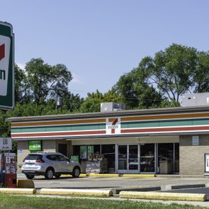 A convenience store with cars parked outside, set in a green, tree-lined environment. A prominent sign reads 