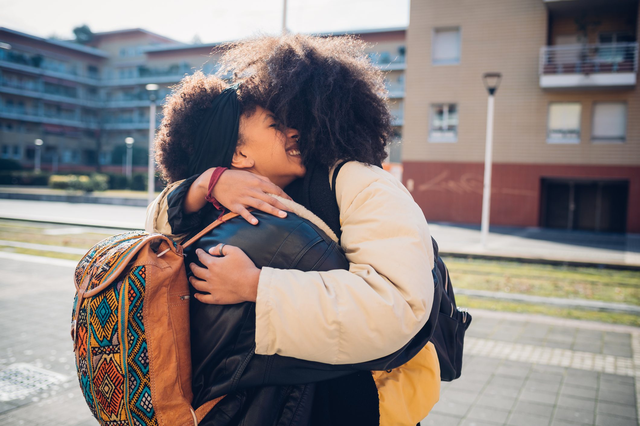Two young women hugging on urban sidewalk