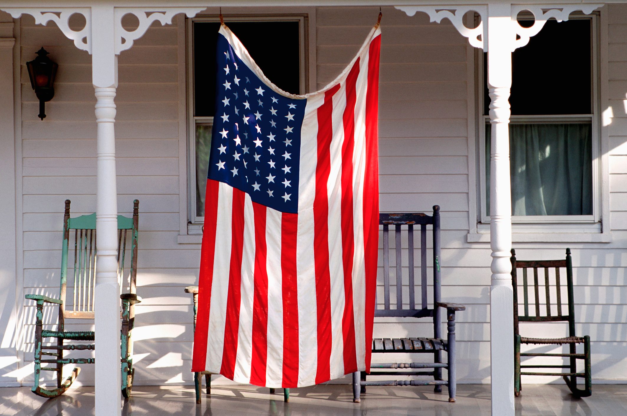 American flag hangs on a porch with three vintage rocking chairs and white wooden siding.