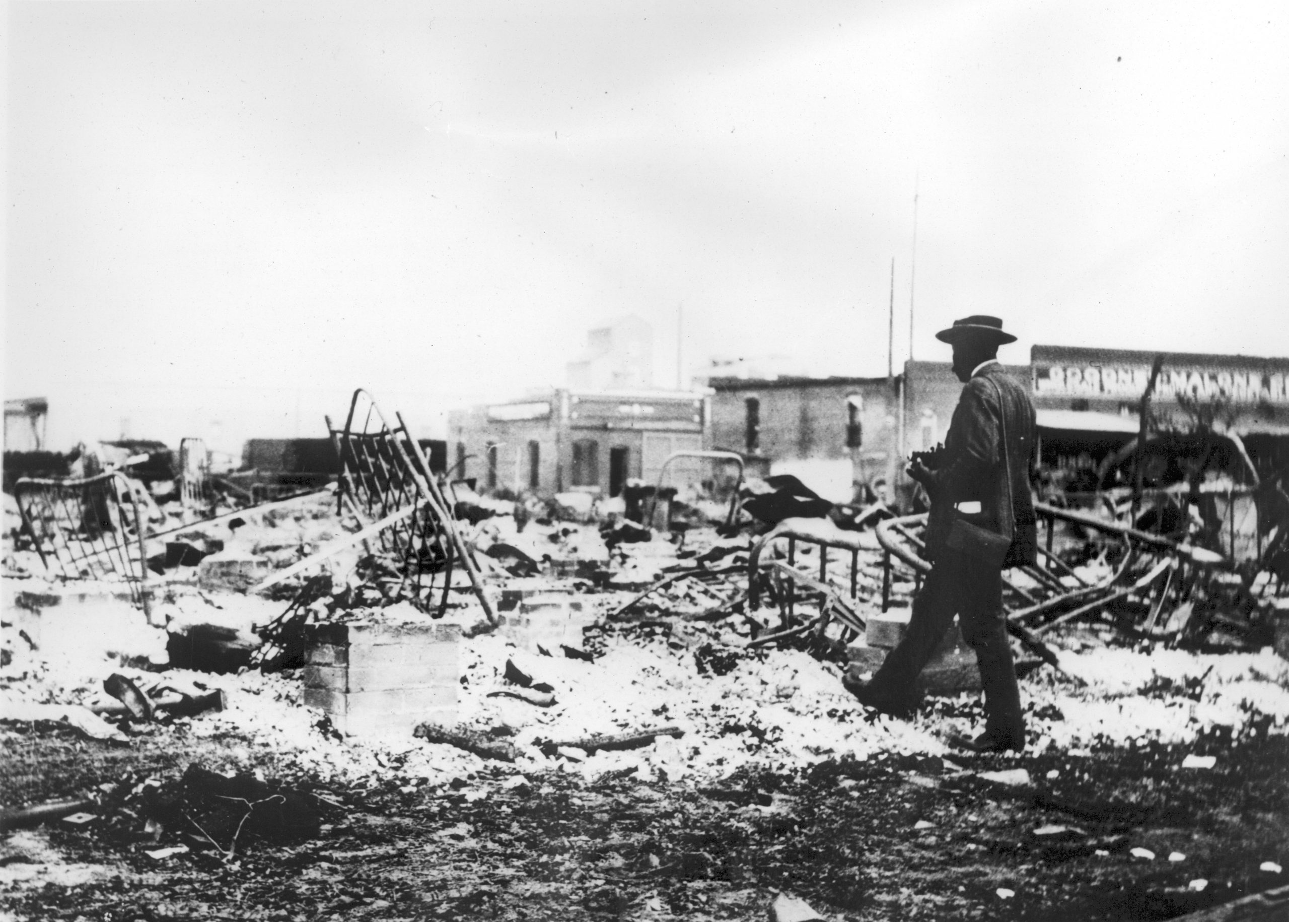 An African-American man with a camera looking at the skeletons of iron beds after the Tulsa Race Massacre