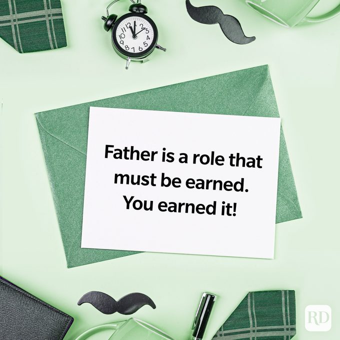 Card rests on green envelope reading, "Father is a role that must be earned. You earned it!" Surrounded by mug, clock, mustache cutouts.