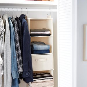Clothes hang neatly in a closet, with folded garments on shelves and a beige storage box, in a well-organized white space.