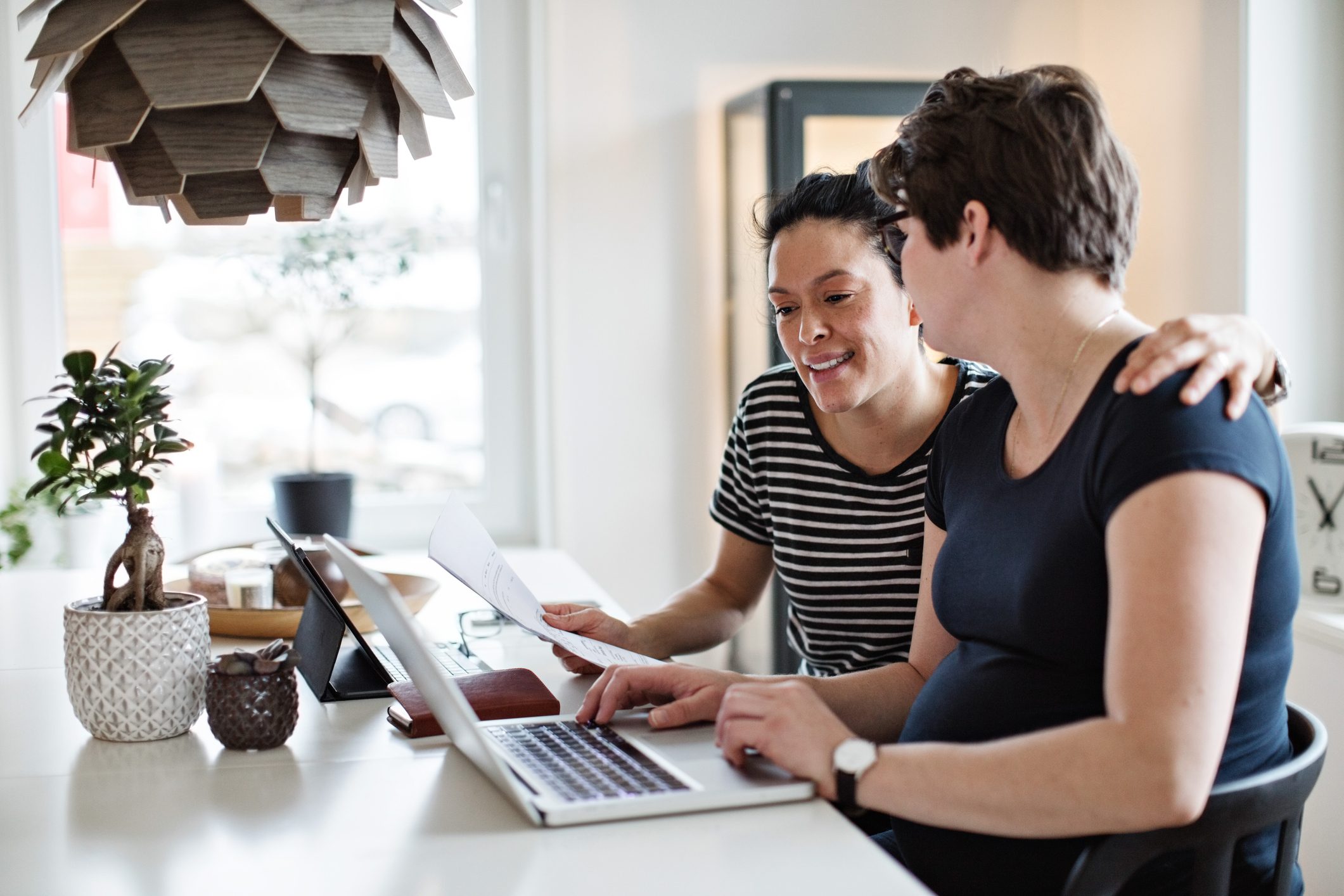 Smiling lesbian couple discussing over bills while using laptop at table