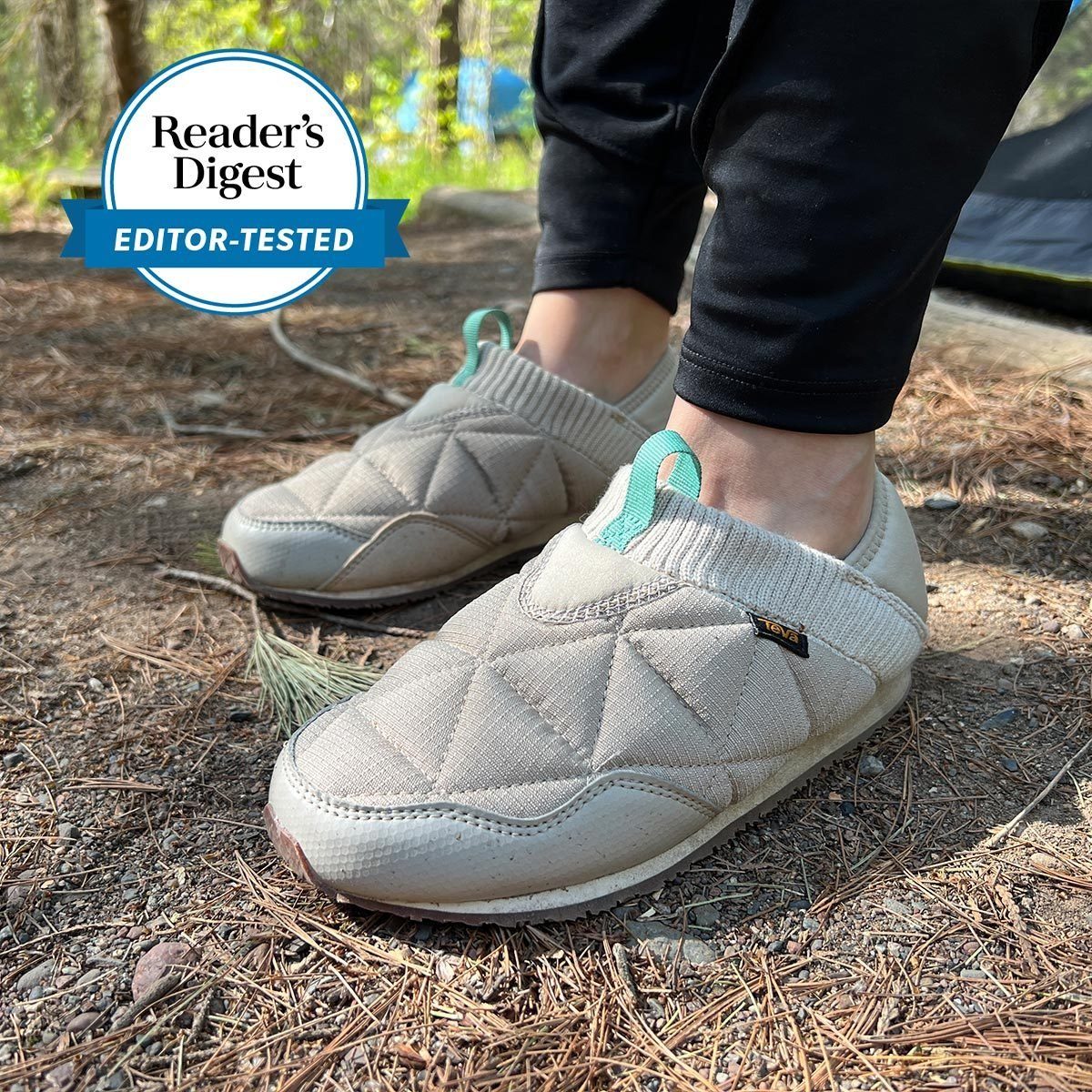 Quilted slippers worn outdoors on a dirt path, surrounded by dry pine needles and greenery, with "Reader's Digest Editor-Tested" badge visible.